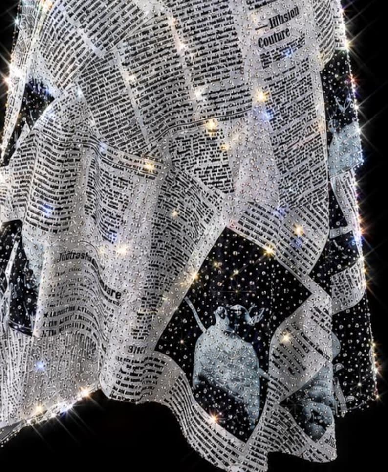 May include: A black and white fabric garment featuring a repeating newspaper print pattern with columns of text and illustrations. The entire surface is densely covered in small, reflective clear crystals that create a sparkling effect.