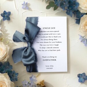 May include: A greeting card with a poem for a godfather, surrounded by cream roses, blue hydrangeas, and a blue ribbon. The card reads "Uncle Ian" and "Thank you being my Godfather."