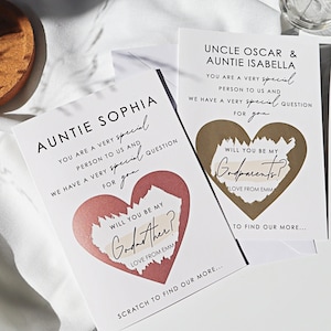 May include: Two white cards with gold and pink hearts. The text on the cards reads "You are a very special person to us and we have a very special question for you."  The text on the hearts reads "Will you be my Godparents?" and "Will you be my Godmother?"  The cards also include the text "Love from Emm" and "Scratch to find our more..."