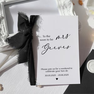 May include: A white rectangular invitation card with black text reading To the soon to be mrs Geeves, Please join us for a weekend to celebrate your hen do, and the dates 30.05.2025 - 01.06.2025, featuring a black frayed ribbon tied on the left side.