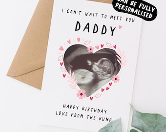 May include: A white card with a pink heart-shaped frame with a black and white ultrasound image inside. The text on the card reads "I can't wait to meet you Daddy. Happy Birthday Love from the Bump."