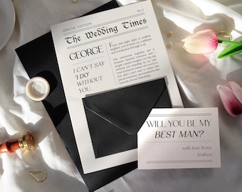 May include: A white card with black text that reads "The Wedding Times" and "George I can't say 'I do' without you..."  A black envelope is behind the card. A smaller white card with black text reads "Will you be my best man? with love from, Nathan".