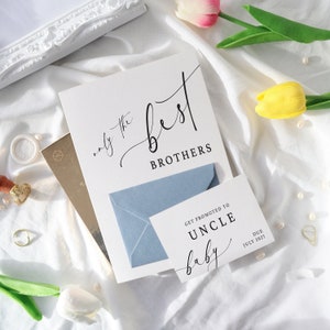 May include: A white card with black text that reads "only the best brothers". A blue envelope is partially covering the card. A smaller white card with black text reads "Get promoted to Uncle baby" and "Due July 2023".