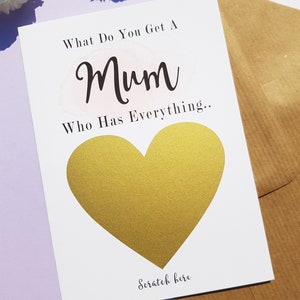 Może przedstawiać: Biała kartka z tekstem "What do you get a Mum who has everything..." i złotym sercem z tekstem "Scratch here" poniżej.