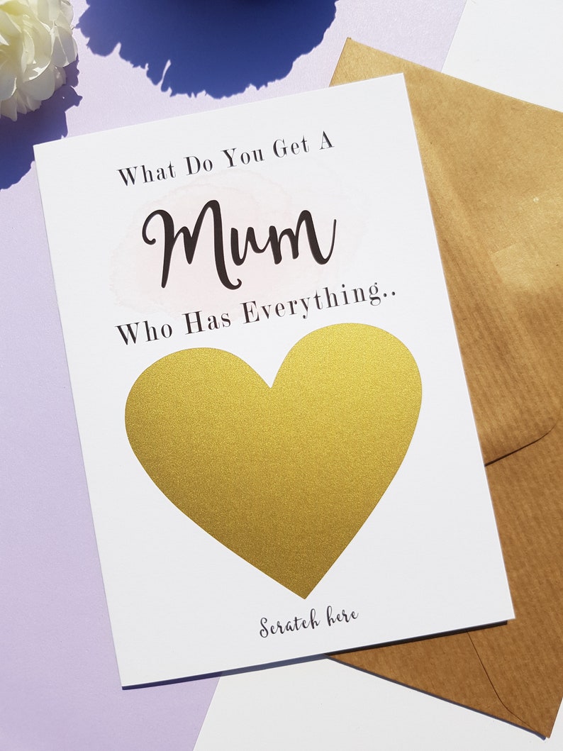 Może przedstawiać: Biała kartka z tekstem "What do you get a Mum who has everything..." i złotym sercem z tekstem "Scratch here" poniżej.
