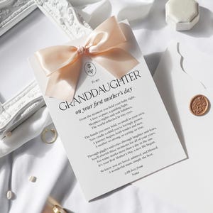 May include: A white card with a peach-colored ribbon tied in a bow. The card has the text "To my GRANDDAUGHTER on your first mother's day" and a poem about motherhood.