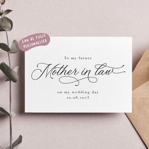 Peut inclure: Une carte blanche avec du texte noir qui dit "To my future Mother in law on my wedding day 10.08.2023". La carte est sur une surface rose avec une plante verte en arri&egrave;re-plan.