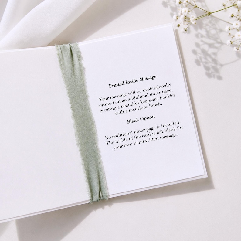 K&ouml;nnte beinhalten: Eine wei&szlig;e Gru&szlig;karte mit einem salbeigr&uuml;nen, ausgefransten Band, das vertikal in der Mitte gebunden ist. Die Karte enth&auml;lt Text, der zwei Optionen erkl&auml;rt: Printed Inside Message mit professionellem Einleger und Blank Option f&uuml;r handschriftliche Notizen.