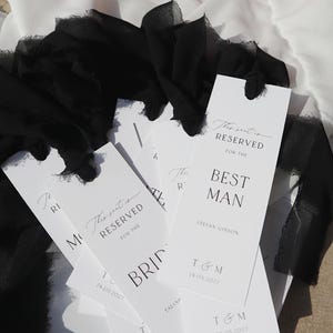 May include: White wedding table place cards with black text. The text reads "This seat is reserved for the Bride" and "This seat is reserved for the Best Man".
