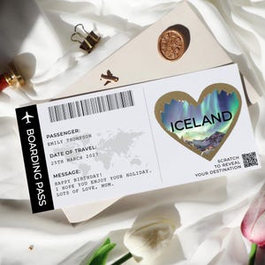 May include: A white and black boarding pass with a gold heart-shaped scratch-off sticker that reveals the destination "ICELAND". The boarding pass has the text "PASSENGER: EMILY THOMPSON DATE OF TRAVEL: 25TH MARCH 2027 MESSAGE: HAPPY BIRTHDAY! I HOPE YOU ENJOY YOUR HOLIDAY. LOTS OF LOVE, MUM."