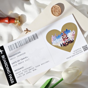 May include: A white boarding pass with a gold heart-shaped scratch-off sticker that says "Disneyland Paris". The boarding pass has the text "Passenger: Emily Thompson", "Date of Travel: 25th March 2027", and "Message: Happy Birthday! I hope you enjoy your holiday. Lots of love, Mum."