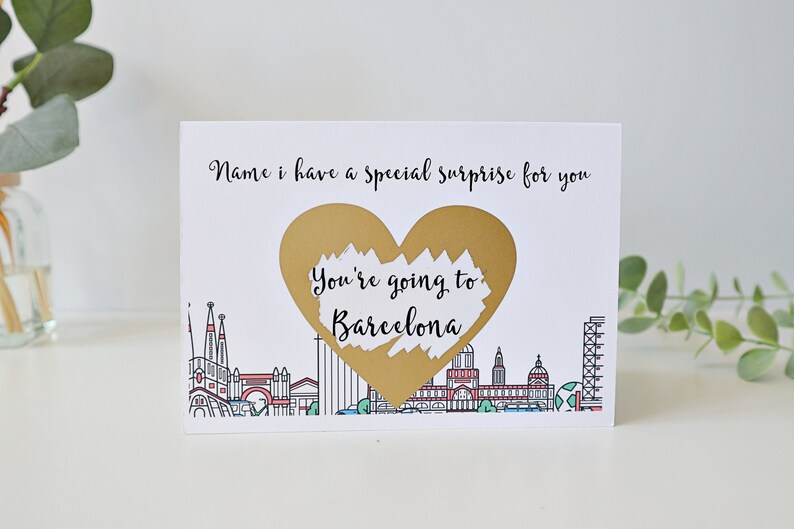 May include: A white card with a gold heart that says "You're going to Barcelona" and a black and white illustration of the Barcelona skyline below.