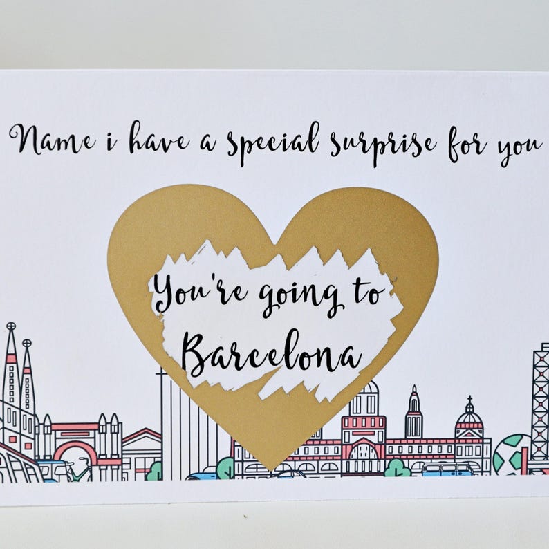May include: A white card with a gold heart shape that says "You're going to Barcelona". The card has a black outline of the Barcelona skyline.