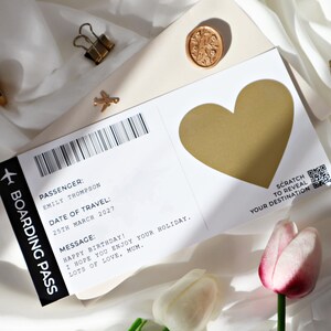 May include: A white boarding pass with a gold heart that can be scratched to reveal a destination. The boarding pass has the text "PASSENGER: EMILY THOMPSON DATE OF TRAVEL: 25TH MARCH 2027 MESSAGE: HAPPY BIRTHDAY! I HOPE YOU ENJOY YOUR HOLIDAY. LOTS OF LOVE, MUM."