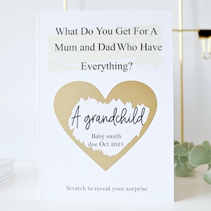May include: A white card with gold foil accents. The card has the text "What Do You Get For A Mum and Dad Who Have Everything?" and a gold heart with the text "A grandchild" and "Baby smith due Oct 2021".