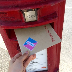 May include: A hand places a brown envelope with a blue and pink sticker that says "WITH PUNS" into a red British post box. The post box has a sign that says "MON" and "Please do not".