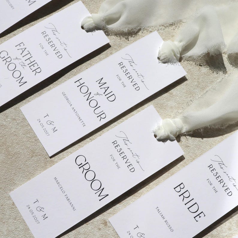 May include: White place cards with black text that reads "This seat is reserved for the" followed by the title of the person the seat is reserved for. The titles include "Maid of Honour", "Groom", and "Bride".