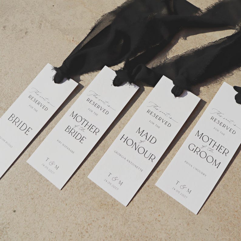 May include: Four white place cards with black calligraphy that reads "This seat is reserved for the" followed by the title of the person the seat is reserved for. The titles are Bride, Mother of the Bride, Maid of Honour, and Mother of the Groom. Each card has the date "24.05.2027" and the initials "T & M" printed on them.