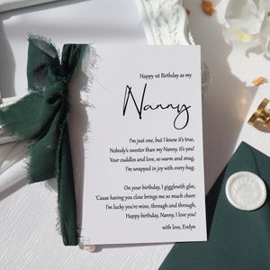 May include: A white card with a green ribbon tied around it. The card has a handwritten message that says "Happy 1st Birthday as my Nanny. I'm just one, but I know it's true, Nobody's sweeter than my Nanny, it's you! Your cuddles and love, so warm and snug, I'm wrapped in joy with every hug. On your birthday, I giggle with glee, 'Cause having you close brings me so much cheer. I'm lucky you're mine, through and through, Happy birthday, Nanny, I love you! with love, Evelyn"