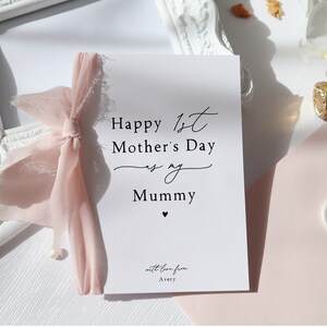 May include: A white card with a pink ribbon tied around it. The card says "Happy 1st Mother's Day as my Mummy" with a small heart at the bottom. The card also says "with love from Avery" at the bottom.
