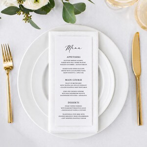 May include: A formal table setting featuring a white plate, folded napkin, and gold cutlery. A menu card with handwritten text is placed on the plate. Floral arrangement in the background. The menu lists appetizers, main courses, and desserts.