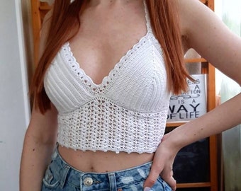 Könnte beinhalten: Weißes Häkel-Halter-Top mit einem zarten, offenen Stichmuster. Das Top ist kurz und hat einen V-Ausschnitt. Das Model trägt das Top zu einer blauen Jeans.