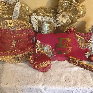 May include: A festive Christmas-themed display featuring a red and gold clock, a personalized pink plaque with the name "ELLIS", and a red ornament. The clock has Roman numerals. The items are decorated with glitter and gold accents.