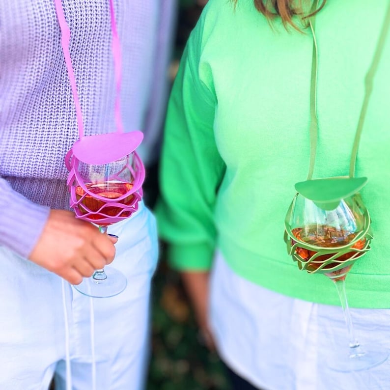 May include: Two people wearing colorful neck straps with wine glasses attached. The straps are made of silicone and have a design that resembles a wine glass. The glasses are filled with red wine.