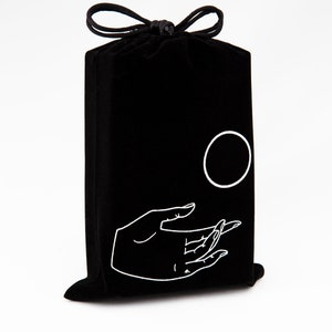 May include: Black velvet drawstring bag with a white hand and circle design. The hand is reaching out towards the circle.