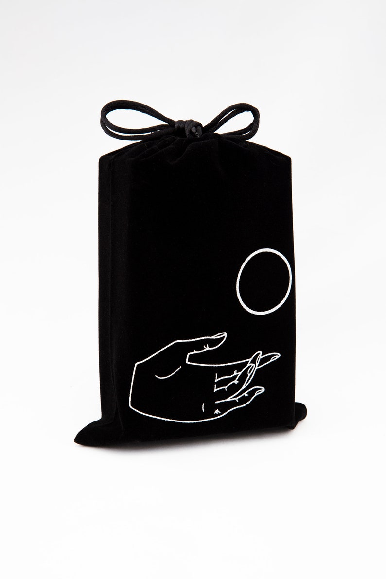 May include: Black velvet drawstring bag with a white hand and circle design. The hand is reaching out towards the circle.