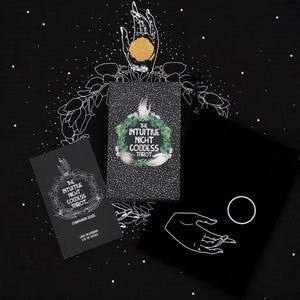 May include: A black velvet bag with a white hand and a circle design. The bag is next to two black and white cards with the text "The Intuitive Night Goddess Tarot" on them. The cards are on a black background with white stars.