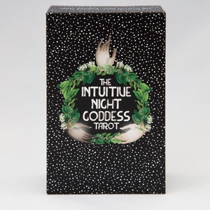 Pu&ograve; includere: Una scatola nera con punti bianchi e una ghirlanda verde con due mani che si protendono. Il testo sulla scatola recita "The Intuitive Night Goddess Tarot".