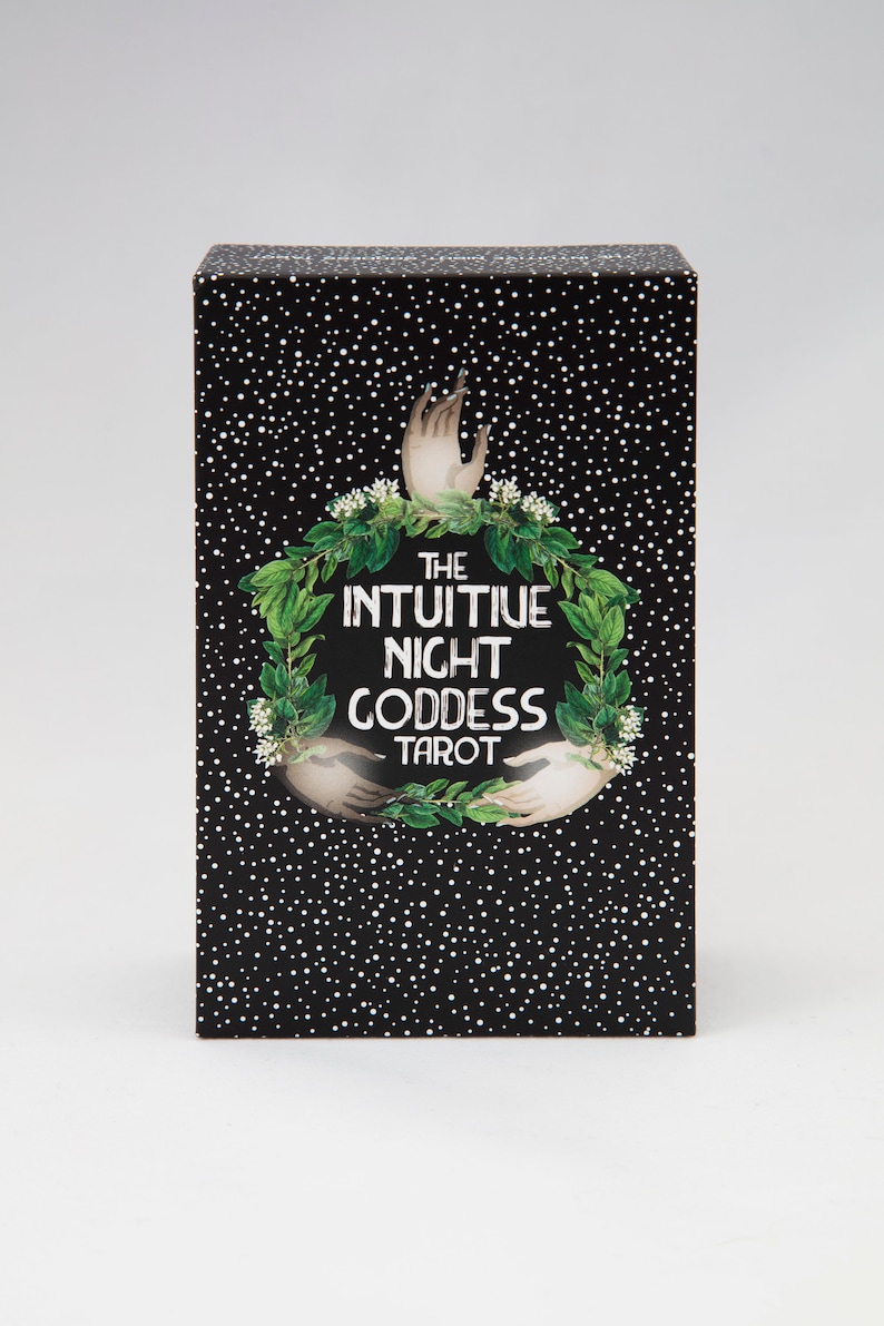 Pu&ograve; includere: Una scatola nera con punti bianchi e una ghirlanda verde con due mani che si protendono. Il testo sulla scatola recita "The Intuitive Night Goddess Tarot".
