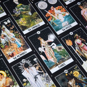 May include: A collection of tarot cards with black borders and various illustrations. The cards feature titles such as "The Witch," "The Monarch," and "The Empress." The artwork includes celestial bodies, figures, and symbolic imagery.