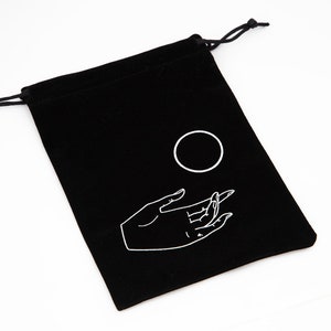 May include: Black velvet drawstring bag with a white hand and circle design. The hand is reaching out towards the circle.