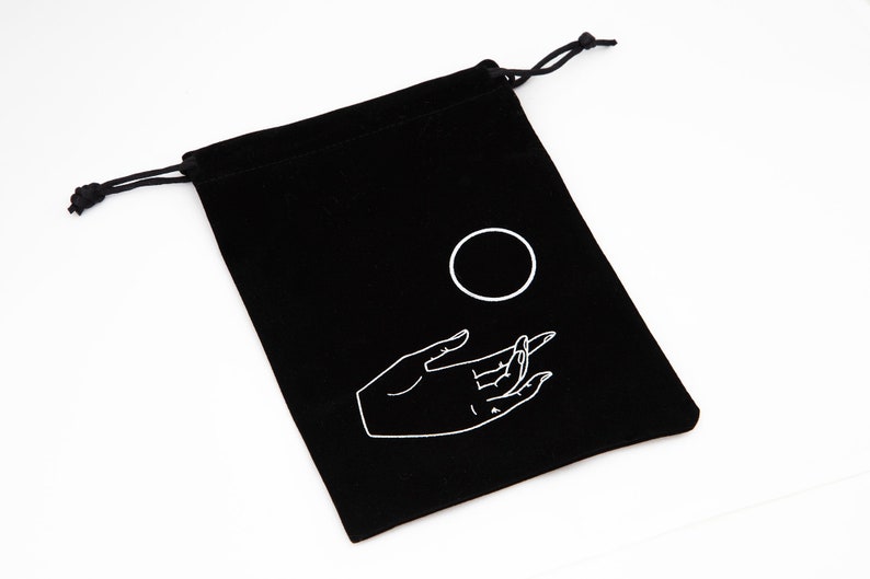 May include: Black velvet drawstring bag with a white hand and circle design. The hand is reaching out towards the circle.