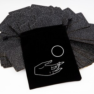 May include: A black velvet bag with a white hand and circle design. The bag contains a deck of black cards with white dots.