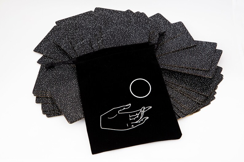 May include: A black velvet bag with a white hand and circle design. The bag contains a deck of black cards with white dots.