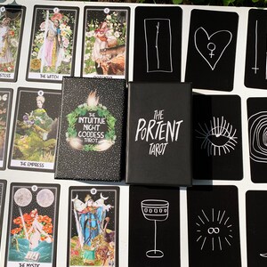 May include: A tarot card deck with a black box featuring the text "THE PORTENT TAROT" and "THE INTUITIVE NIGHT GODDESS TAROT". The cards are black with white illustrations and text, including "THE HIGH PRIESTESS" and "THE EMPRESS".