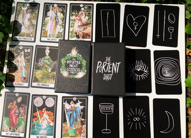 May include: A tarot card deck with a black box featuring the text "THE PORTENT TAROT" and "THE INTUITIVE NIGHT GODDESS TAROT". The cards are black with white illustrations and text, including "THE HIGH PRIESTESS" and "THE EMPRESS".