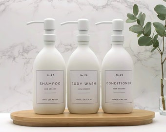 May include: Three white pump bottles with labels reading "No. 27 Shampoo 100% Organic", "No. 28 Body Wash 100% Organic", and "No. 29 Conditioner 100% Organic" on a wooden tray.