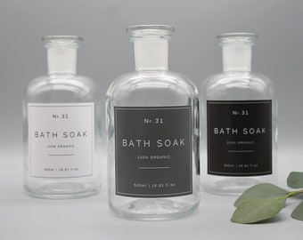 Può includere: Tre bottiglie di vetro trasparente con etichette nere che recitano "No. 31 Bath Soak 100% Organic 500ml | 16.91 fl oz". Le bottiglie sono su uno sfondo grigio.