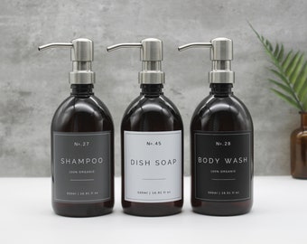 May include: Three amber glass bottles with black labels and silver pump tops. The labels read "No. 27 Shampoo 100% Organic", "No. 45 Dish Soap", and "No. 28 Body Wash 100% Organic". Each bottle is 500ml or 16.91 fl oz.