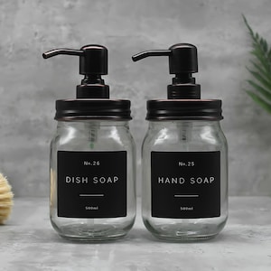 May include: Two glass soap dispensers with black labels and bronze lids. The dispenser on the left says "No. 26 DISH SOAP 500ml" and the dispenser on the right says "No. 25 HAND SOAP 500ml".