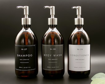 May include: Three amber glass bottles with silver pump tops and black labels. The labels have white text that reads "No. 27 Shampoo 100% Organic", "No. 28 Body Wash 100% Organic", and "No. 29 Conditioner 100% Organic". Each bottle is 500 ml or 16.91 fl oz.