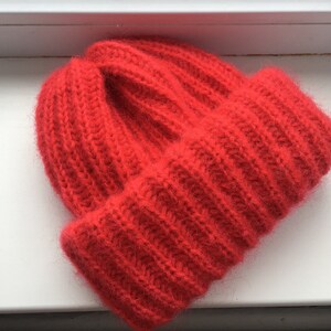 May include: A vibrant red knit beanie hat with a folded brim. The hat is made of a soft, textured material and features a ribbed design. The hat is a winter accessory.