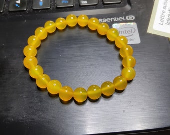 May include: A yellow beaded bracelet made of round, smooth stones. The bracelet is lying on a black laptop keyboard.