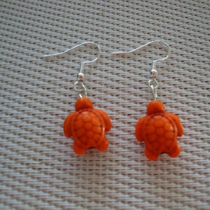 May include: A pair of silver earrings with orange turtle charms. The turtles have a textured shell design.