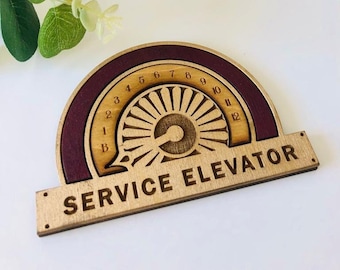 May include: A wooden sign with the text "SERVICE ELEVATOR" in brown lettering. The sign has a circular design with a red border and a wood-grain background. The circle has numbers 1 through 12 and a stylized design of a wheel.