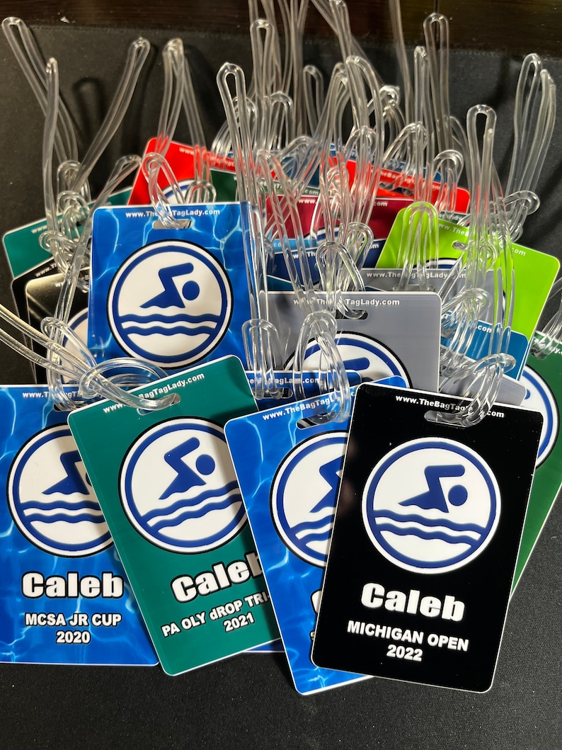 May include: A collection of colorful luggage tags with clear plastic loops. Each tag features a swimmer graphic within a white circle, with the text "Caleb" and event details like "MCSA JR CUP 2020" and "MICHIGAN OPEN 2022".